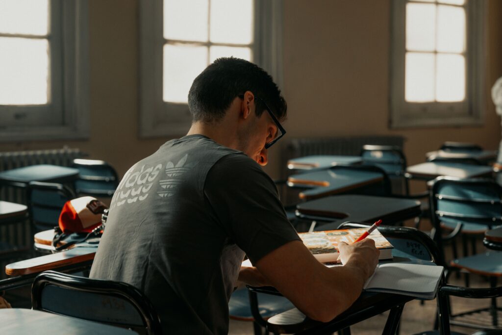 Focused student studying in empty classroom with warm natural light streaming through windows.